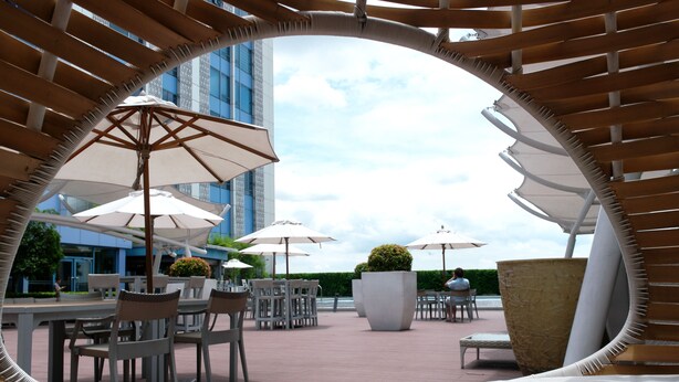 An outdoor seating area with tables and chairs, surrounded by umbrellas, and overlooking a body of water. - Posh Entrata SOHO Suite-- Festival Mall view (Alabang, Muntinlupa City)