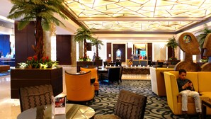 A lobby with a geometric ceiling design, seating areas, and a central decorative column. - Posh Entrata SOHO Suite-- Festival Mall view (Alabang, Muntinlupa City)