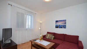 Ein Wohnzimmer mit einem Holztisch, einem roten Sofa, einem Fernseher auf einem Schrank und einem Gemälde an der Wand.