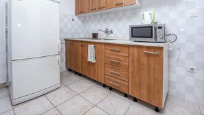 A kitchen with a white refrigerator, wooden cabinets, a microwave, and a tiled backsplash. - Apartments Karleusa (Rogoznica)