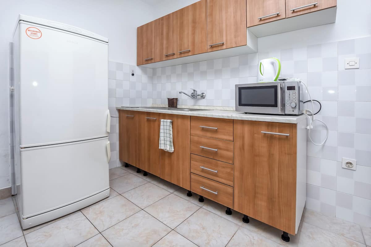 A kitchen with a white refrigerator, wooden cabinets, a microwave, and a tiled backsplash.