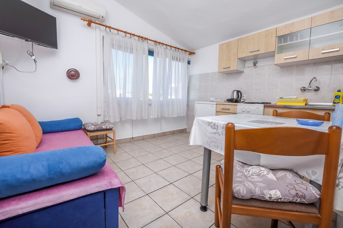 A compact kitchen with a dining table, a sofa, and a TV mounted on the wall.