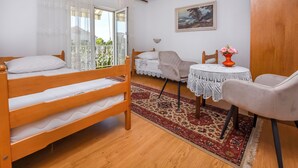 A bedroom with a wooden bunk bed, a small table with a lace tablecloth, a chair, and a window with sheer curtains. - Apartments Karleusa (Rogoznica)