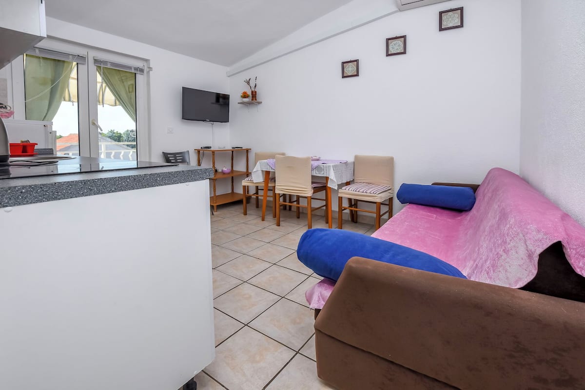 A compact living space with a kitchenette, dining area, and a sofa with cushions.