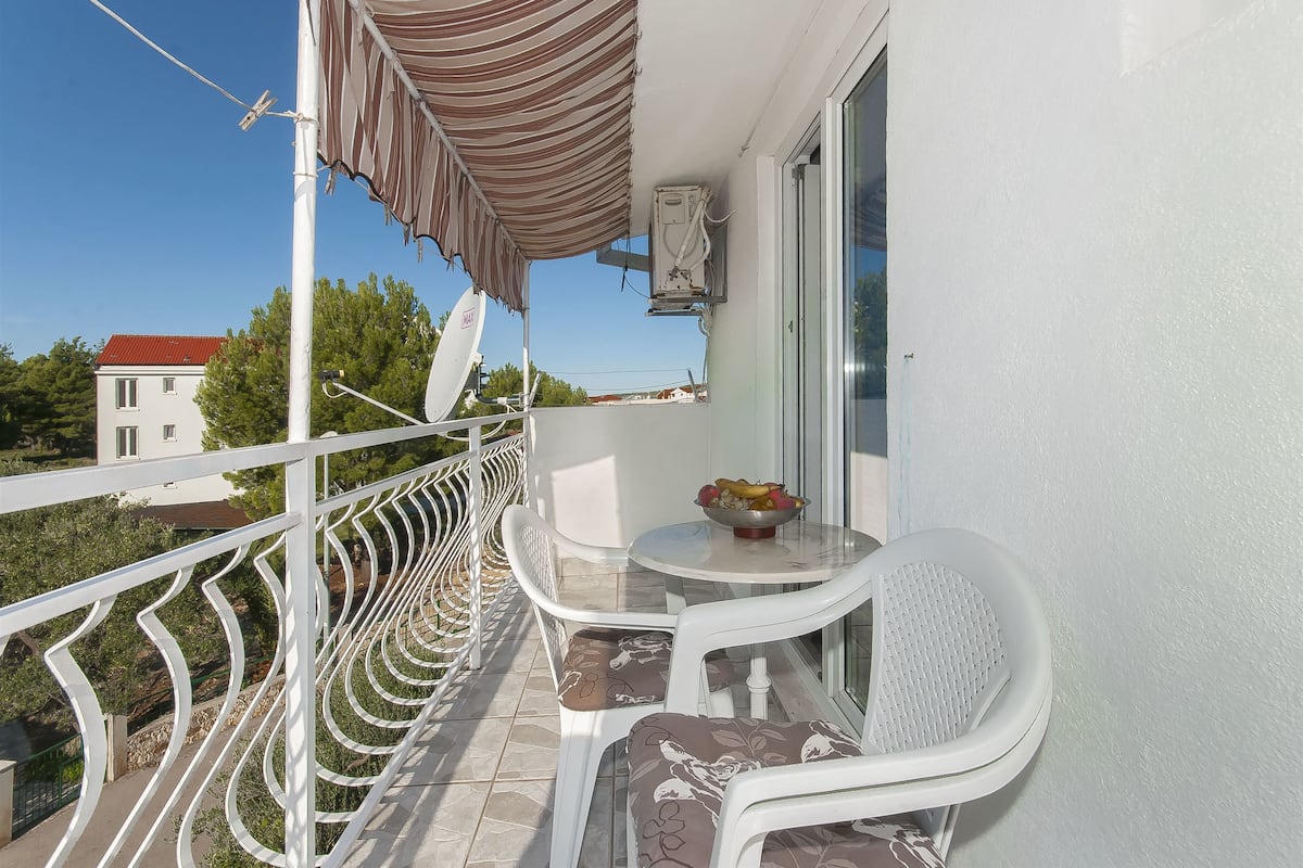 A balcony with white chairs, a small table with a bowl of fruit, and a satellite dish.