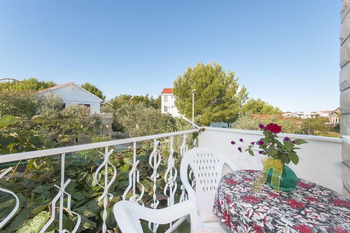 A balcony with a white railing, a chair with a floral cushion, and a vase with flowers.