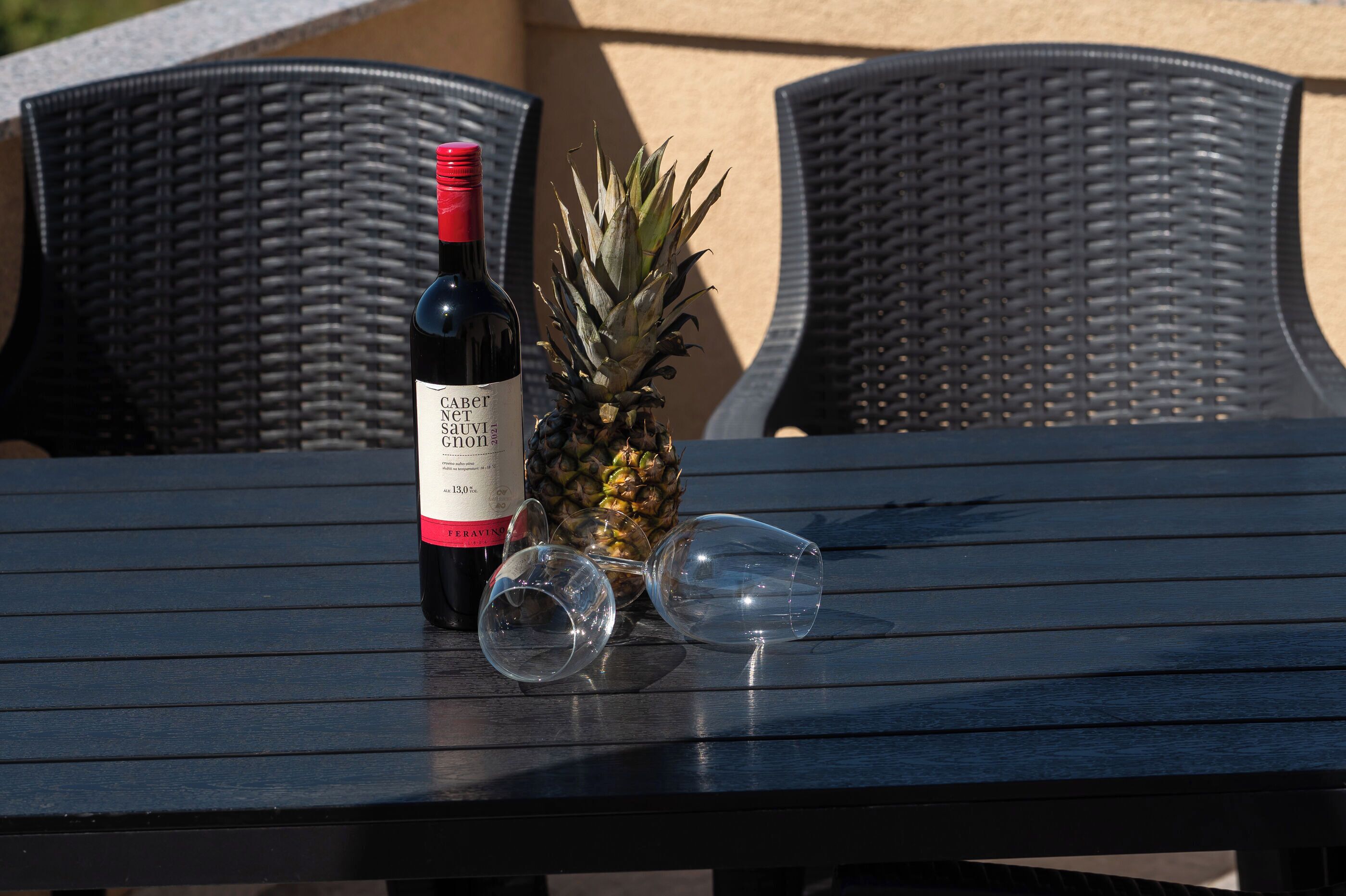 Une table avec une bouteille de vin rouge, un ananas et deux verres à vin vides.
