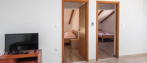 Een kamer met een televisie op een houten standaard, een bed met een roze kussen, en een houten deur die naar een andere kamer leidt.