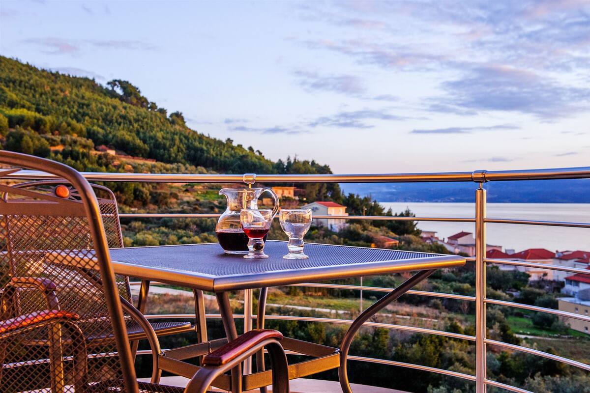 Ein Balkon mit Tisch für zwei Personen, ausgestattet mit einer Weinflasche und Gläsern, mit Blick auf eine malerische Landschaft mit Wasserspiegel und Hügeln.