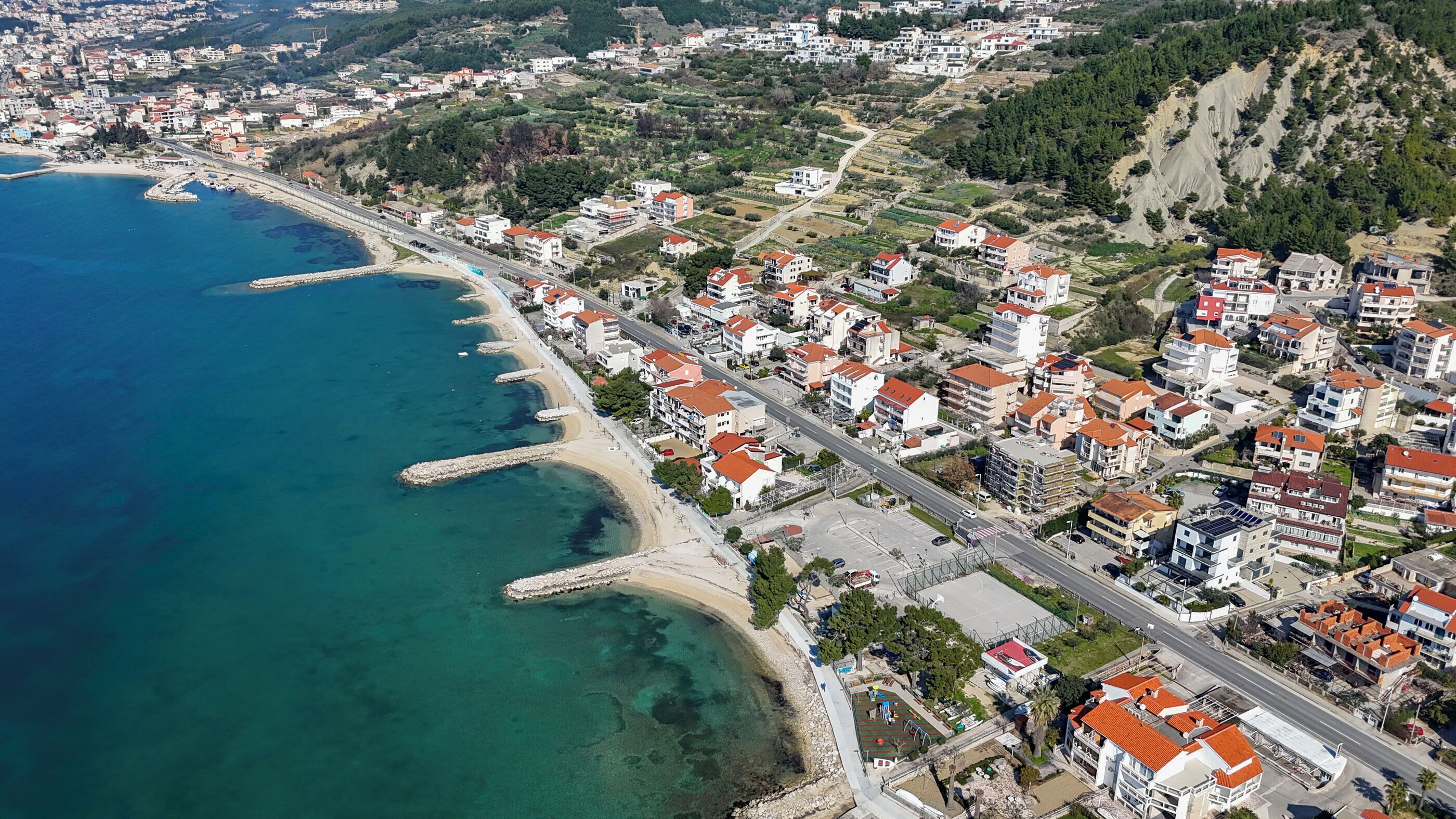 An aerial view of a coastal town with a beach, residential buildings, and a road.