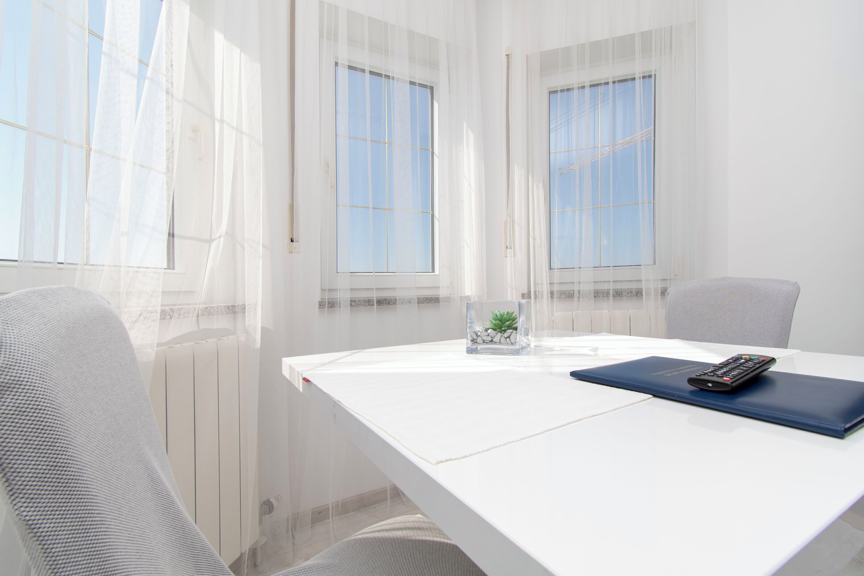 A white table with a remote control and a blue folder, two chairs, and a small plant on a white table.
