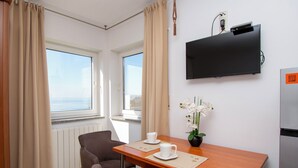 A hotel room with a wooden table, two chairs, a TV, a flower vase, and a view of the sea. - Apartment and Rooms Ana (Podstrana)