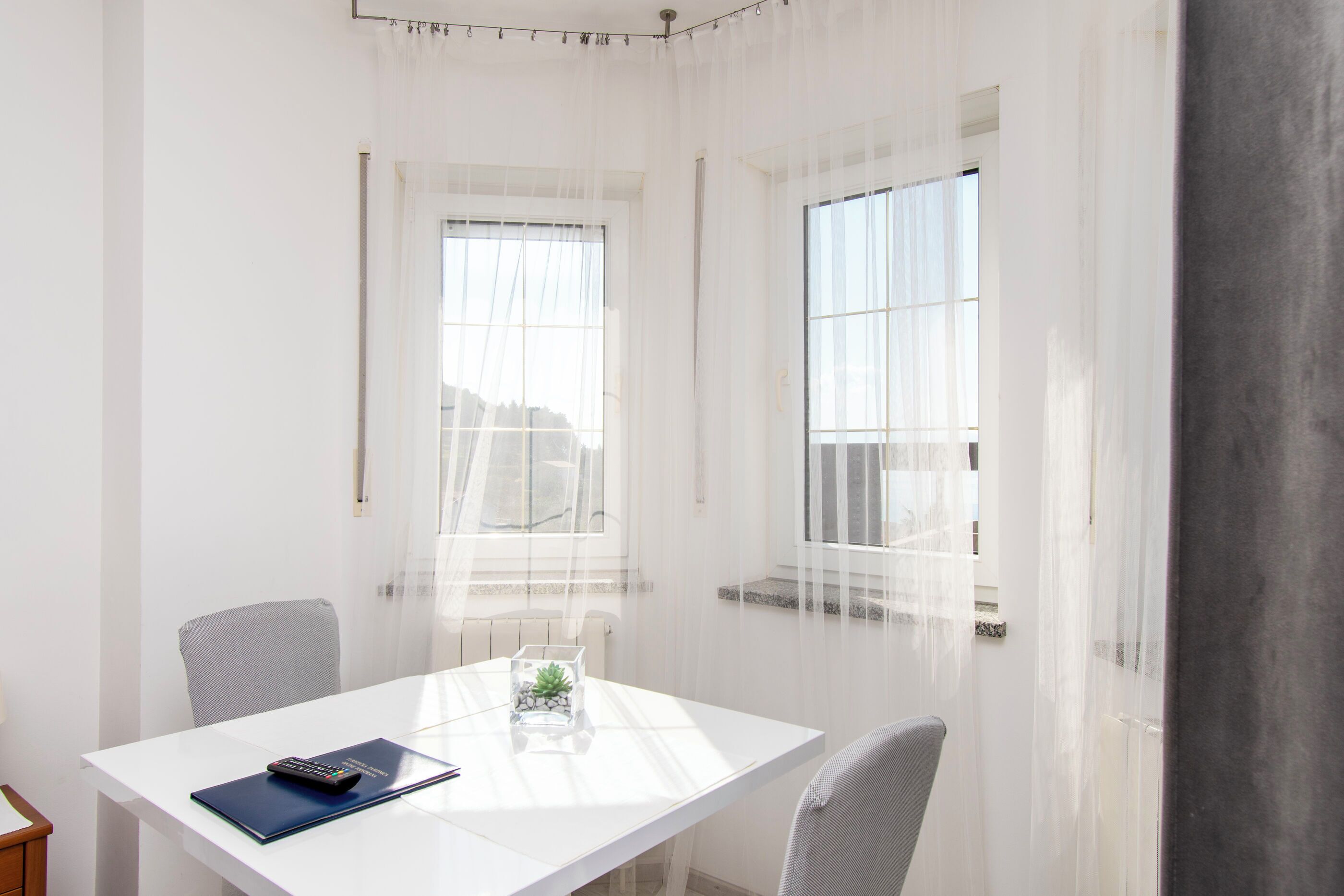 A room with a white table, two chairs, a small plant, and a remote control.