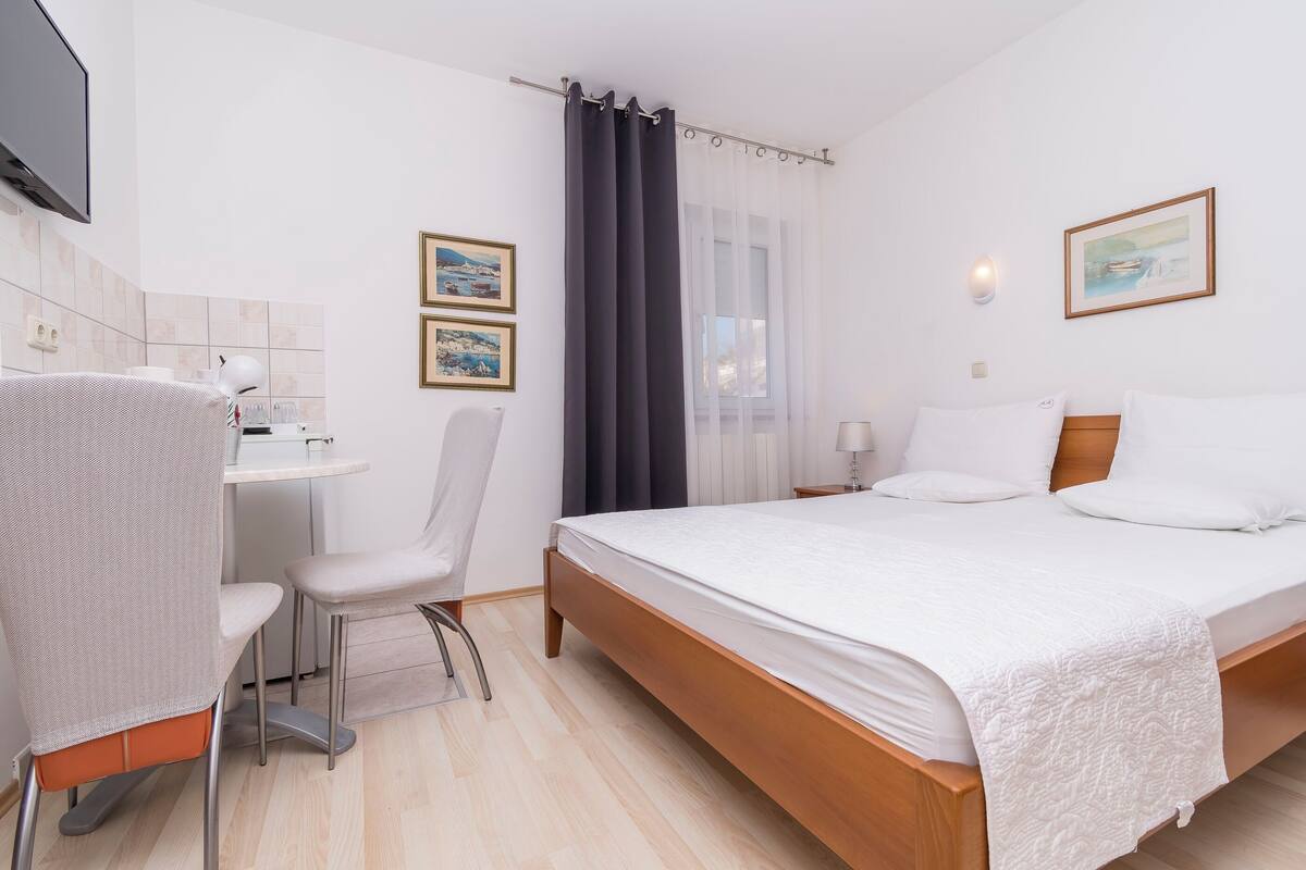 Ein Hotelzimmer mit Bett, Schreibtisch, Sessel, Fernseher und einem fensterbepflanzten Fenster.