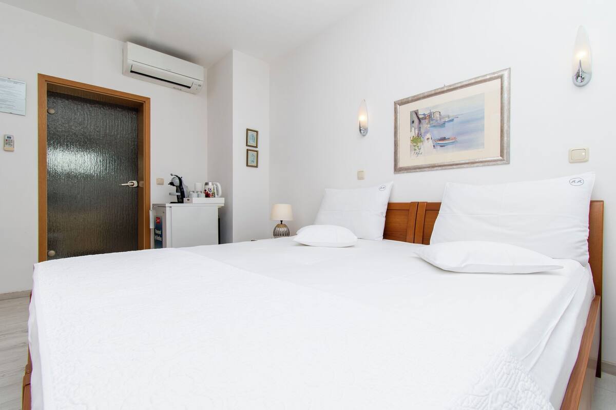 Ein Hotelzimmer mit einem Bett, einem Schreibtisch, einem Sessel, einer Klimaanlage, einer Wandleuchte und einem gerahmten Bild.