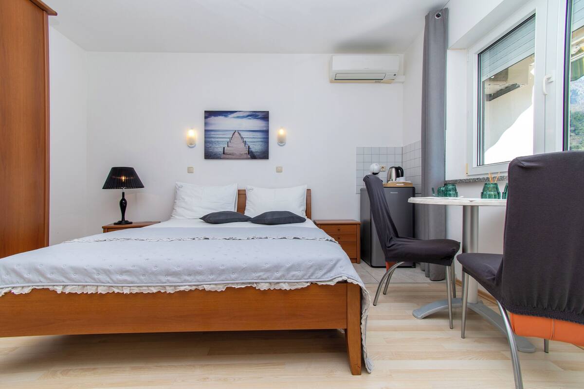 Ein Schlafzimmer mit Bett, Schreibtisch und Stuhl, ein Fenster mit Blick und eine Klimaanlage.