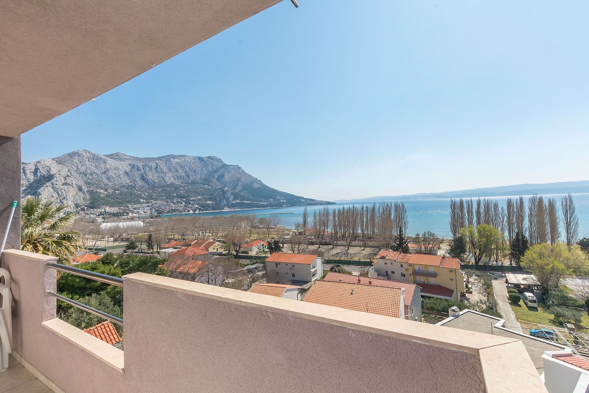 A balcony with a view of a coastal town, mountains, and a body of water.