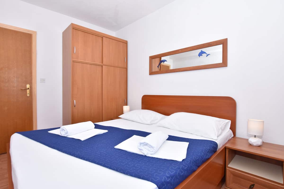 A hotel room with a wooden bed, white pillows, a blue bedspread, and a wooden wardrobe.