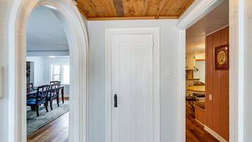 Um corredor com porta branca, piso de madeira e um arco que dá para uma sala de jantar.