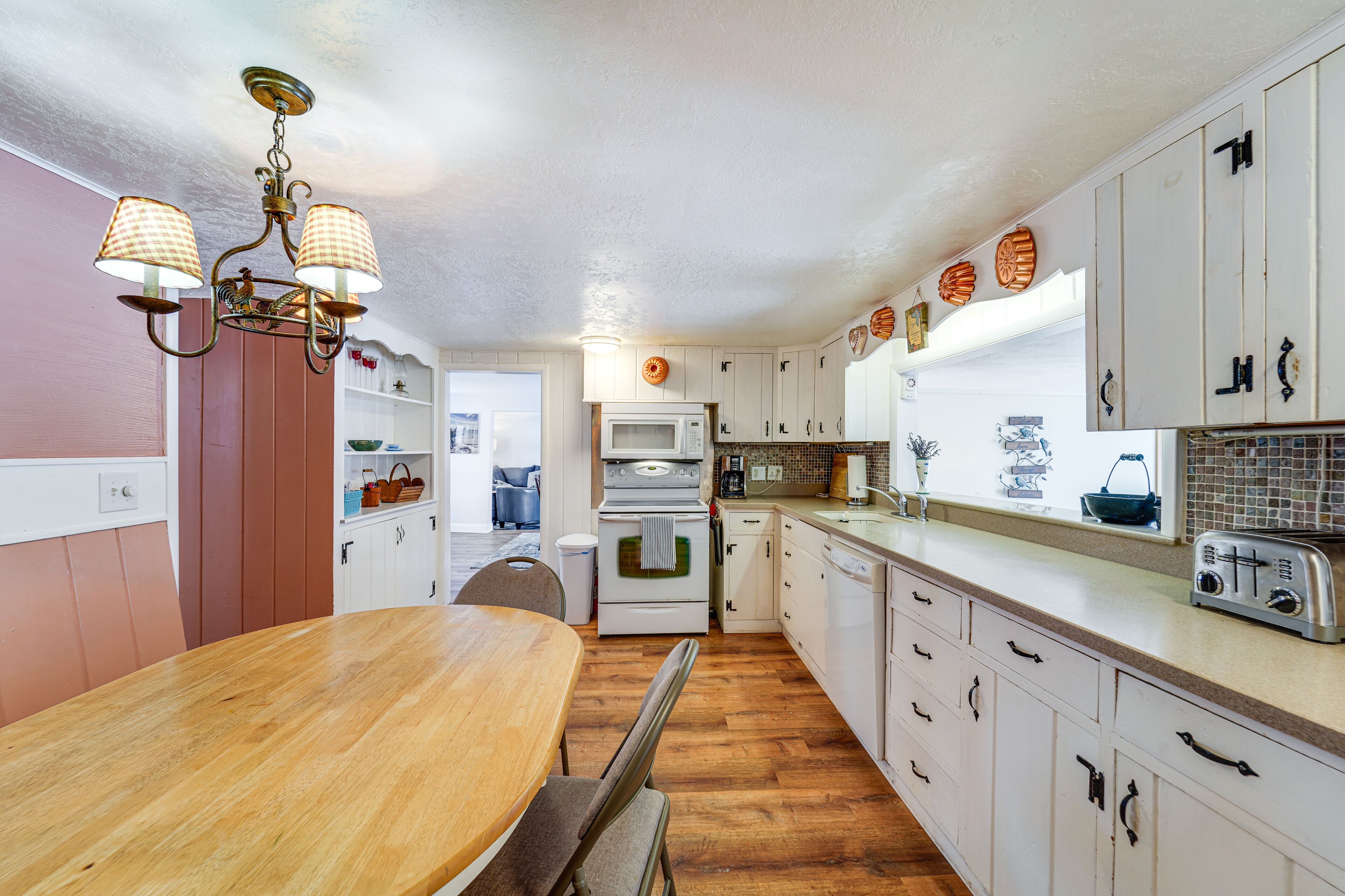 Una cocina con armarios de madera, encimera blanca, mesa de comedor de madera y una araña.