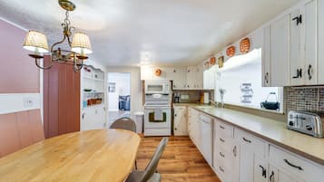 Una cocina con armarios de madera, encimera blanca, mesa de comedor de madera y una araña.