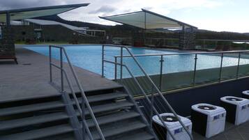 A swimming pool with steps leading down to the water, a stone building in the background, and a clear sky.