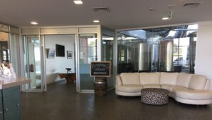 Un interior moderno con entrada por puerta de cristal, un sofá de cuero blanco, un reposapiés estampado y un letrero que indica cafetería y bar.