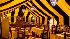 Un'area pranzo allestita con tende, tavoli, sedie, lampadari e un armadio.