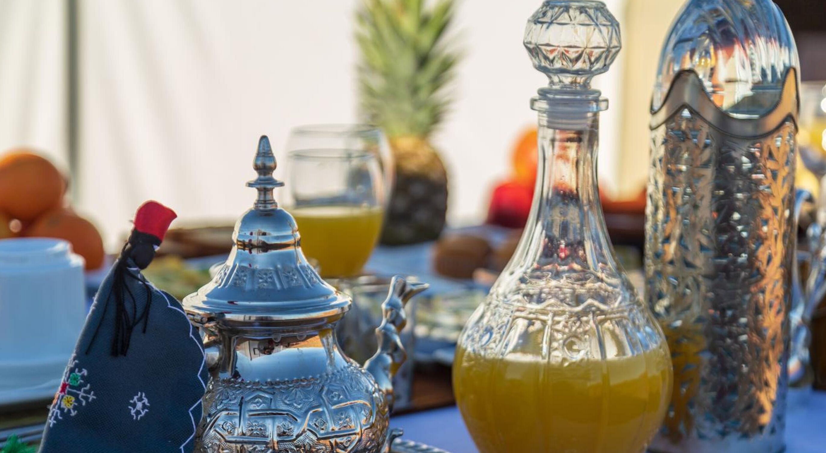 Una mesa dispuesta con cubertería ornamentada, un vaso de jugo de naranja y una piña.