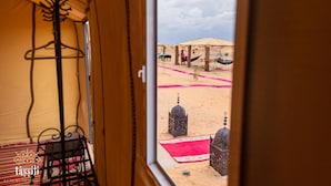 Un campo nel deserto con una tenda, un appendiabiti sospeso e un tappeto rosso.