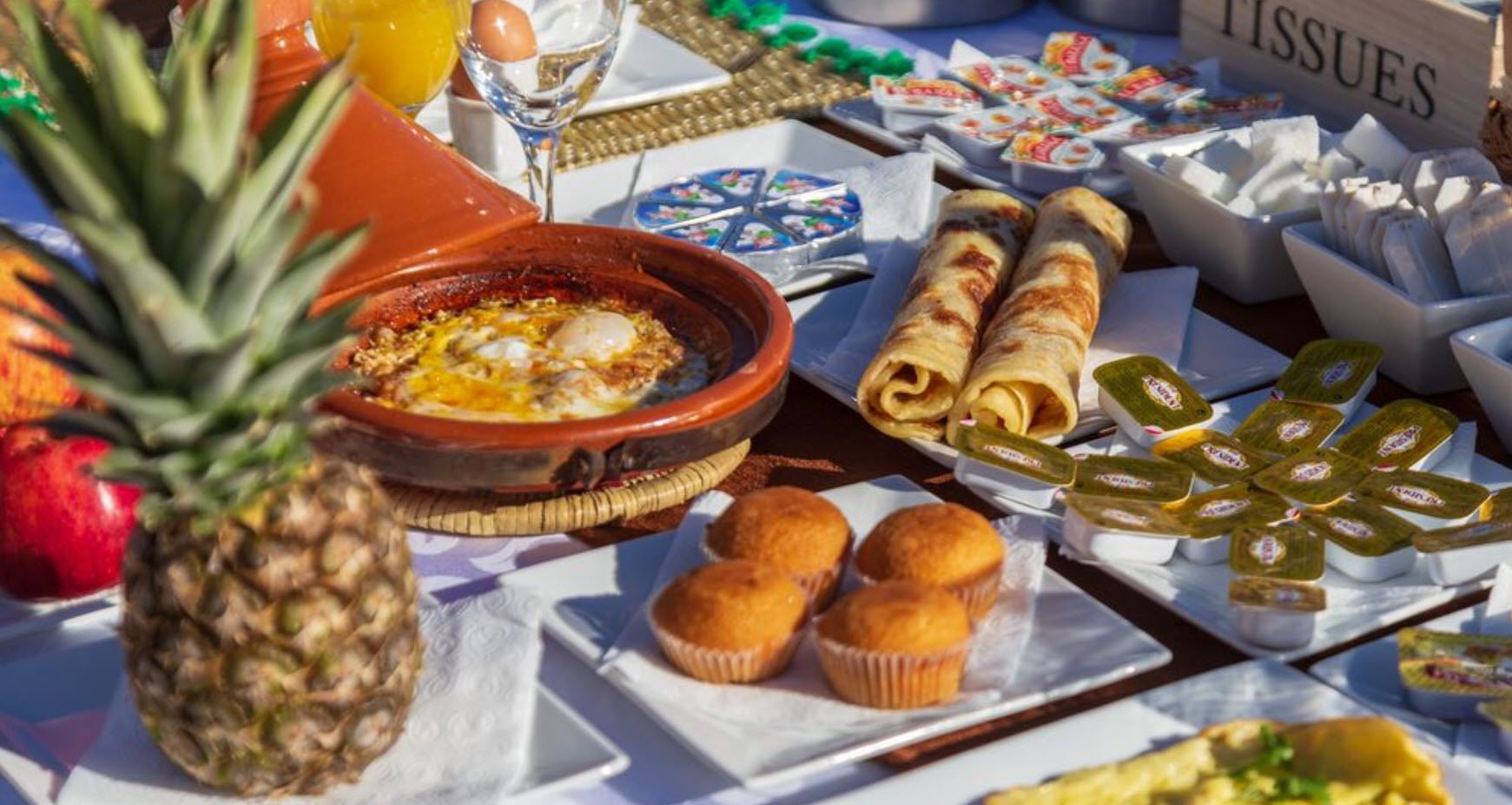 A breakfast buffet with various food items including pastries, a pineapple, and a dish with eggs.