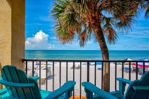A balcony with turquoise chairs overlooking a beach with umbrellas and people. - Beachfront Balcony Corner Unit on Madeira Beach. Updated, Comfortable 1st Floor, with Pool & Grill. (Madeira Beach)