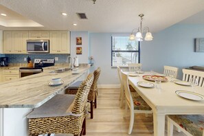 Uma cozinha moderna com ilha central, armários brancos e uma área de jantar com mesa e cadeiras brancas.
