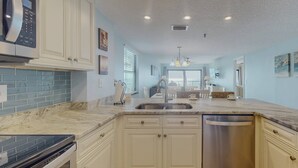 A modern kitchen with white cabinetry, a stainless steel dishwasher, and a marble countertop. - Beachfront Balcony Corner Unit on Madeira Beach. Updated, Comfortable 1st Floor, with Pool & Grill. (Madeira Beach)