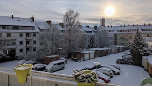Un quartiere residenziale con auto e edifici innevati, cielo sereno e il sole che tramonta o sorge.