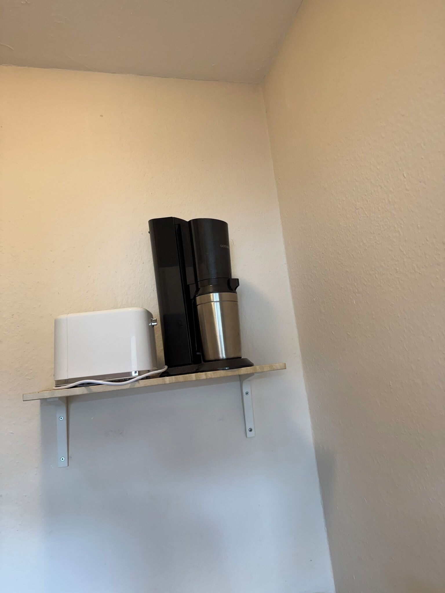 A white wall with a shelf holding a coffee maker and a white appliance.