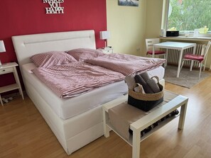 Un dormitorio ordenado con una cama, mesitas de noche, una pequeña mesa y una silla.