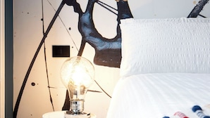 A bedroom with a bed, a nightstand, a wall mural, and a light bulb.