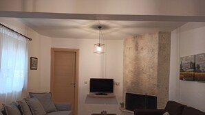 A living room with a sofa, a coffee table, a TV mounted on a stone wall, and a fireplace. - Il Silenzio   ground floor (Magarikari)