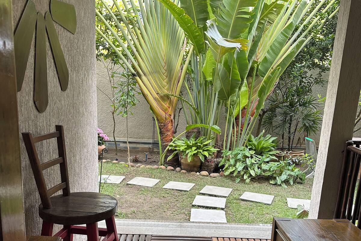 A wooden bench and chair arrangement in a covered outdoor area with a view of a garden.