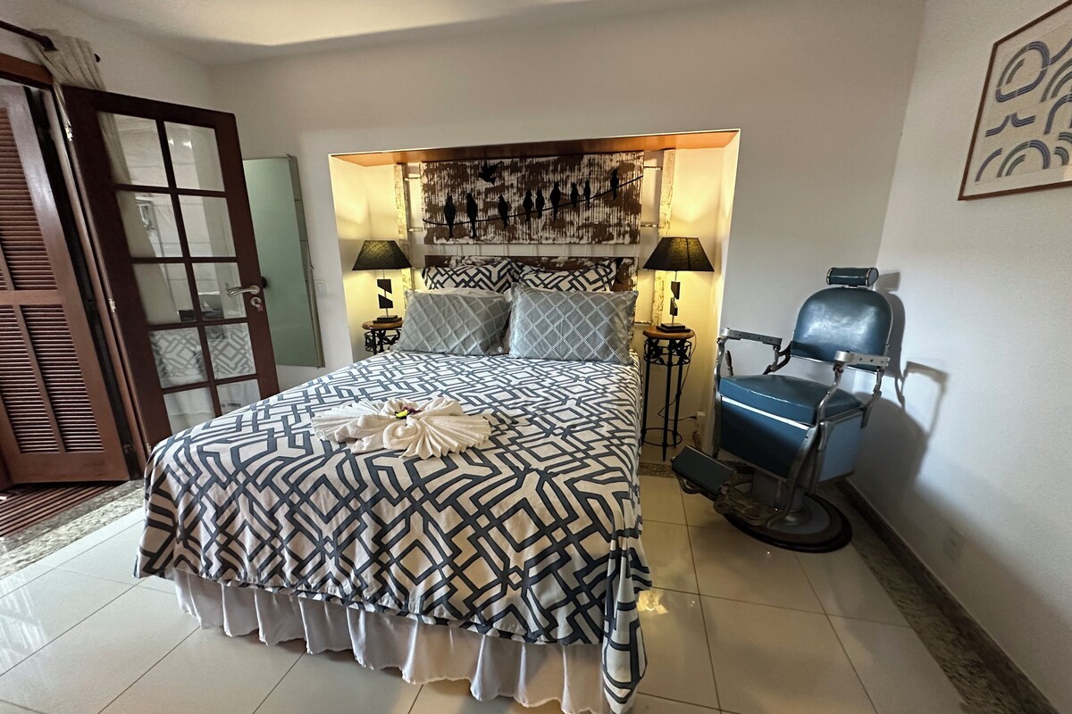 A hotel room with a large bed, two bedside lamps, a blue chair, and a decorative headboard.