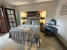 Una habitación de hotel con una cama grande, dos lámparas de noche, un sillón azul y un cabecero decorativo.