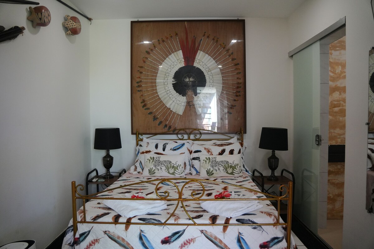 A bedroom with a bed, two bedside tables, a wall-mounted lamp, and a decorative wall piece.