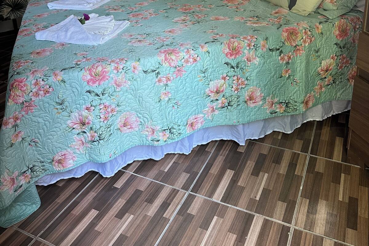 A neatly made bed with floral bedding, a wall with three framed pictures, and a wooden floor.