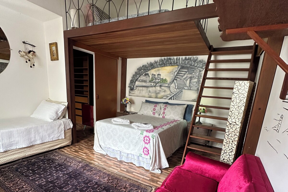A bedroom with a bed, a red sofa, a wooden floor, a staircase, and a mural on the wall.