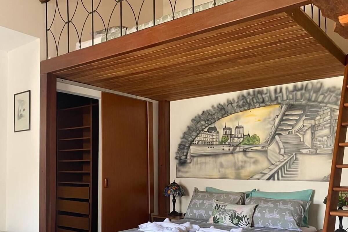 A bedroom with a bunk bed, a bed with a patterned bedspread, a colorful rug, and a mural of a cityscape on the wall.