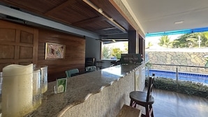 A reception area with a marble counter, wooden panel walls, a framed artwork, and a view of the outdoors. - Hotel Flor De Limao (Santa Cruz Cabralia)