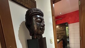 A hallway with a wooden door frame, a black pedestal with a Buddha statue, a red wall, and a tiled floor. - Hotel Flor De Limao (Santa Cruz Cabralia)