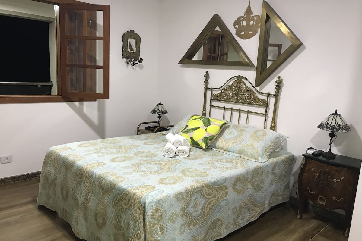 A neatly made bed with patterned bedding, a bedside lamp, and a nightstand with a lamp.