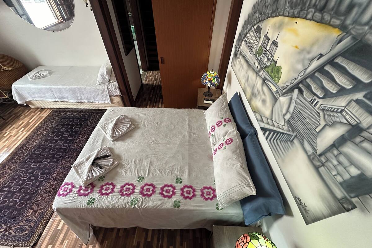 A small, cozy room with a bed, a rug, and a painting of a bridge.